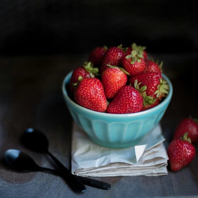 the bowl contains strawberries and is next to a plastic spoon