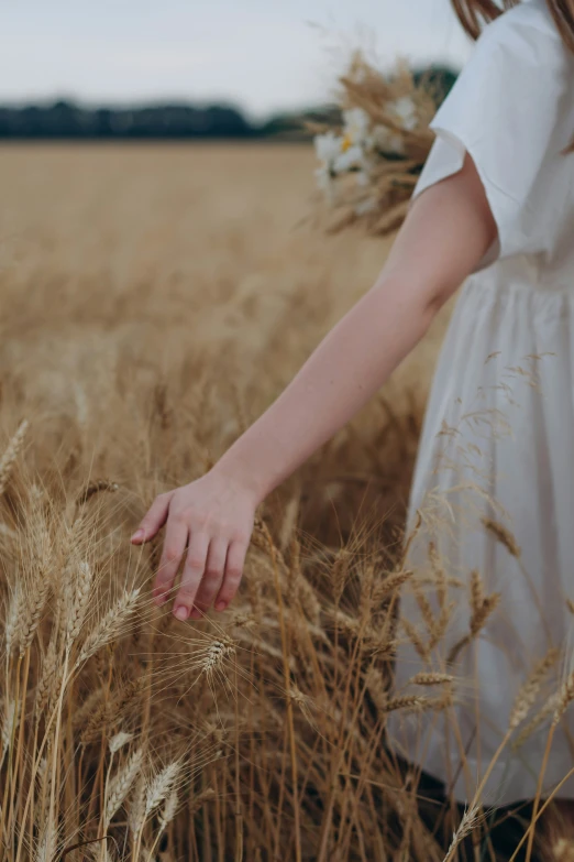 a woman in a white dress and pink shoes is walking through some tall grass