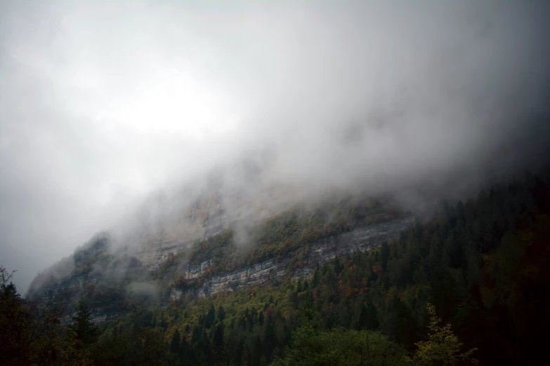 a mountain covered in clouds and trees under a cloudy sky