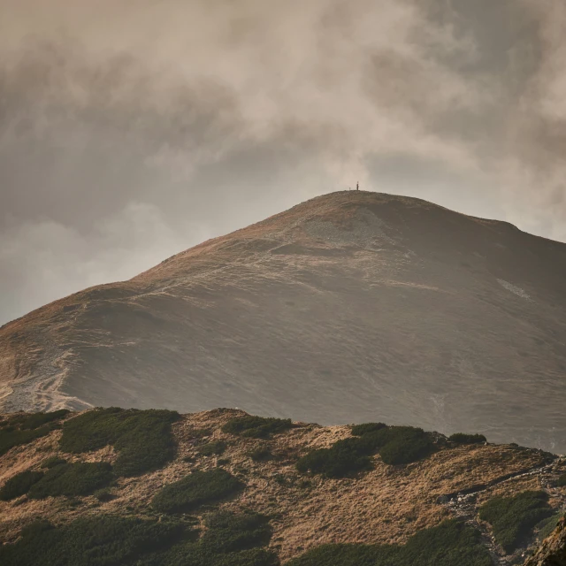 clouds move in the air as there is a lone tree on top of the mountains