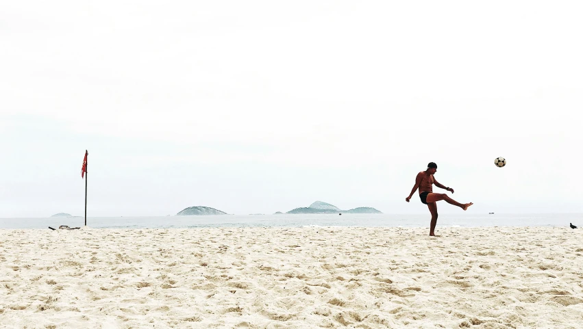 a man kicking a ball on a sandy beach