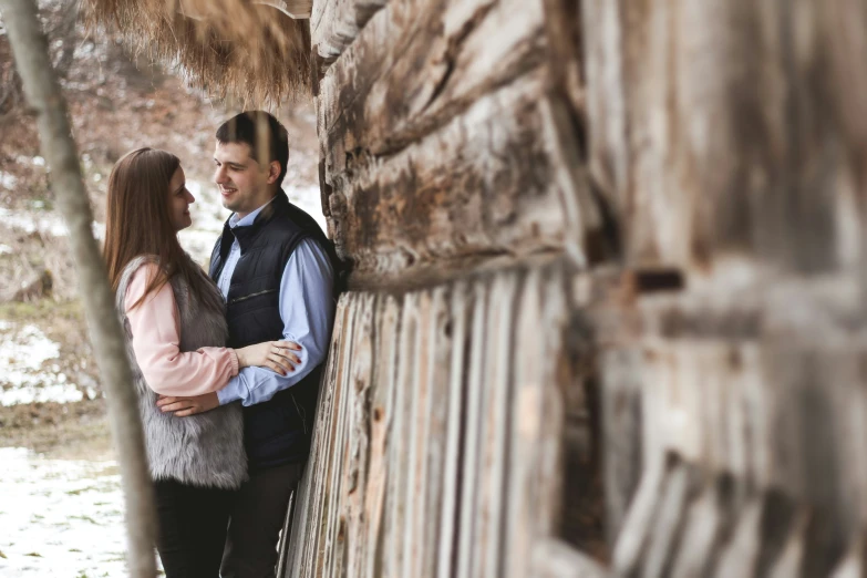 a couple hugging and standing near some old wood