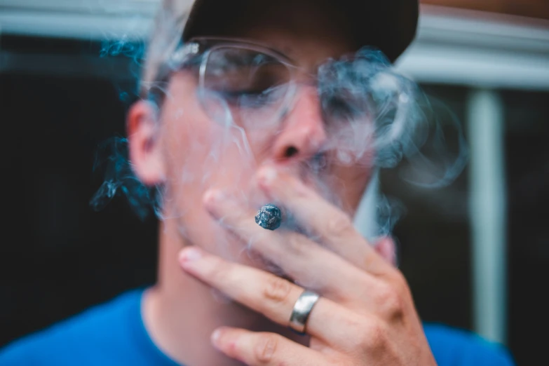 man smoking electronic cigarette with hat and blue shirt