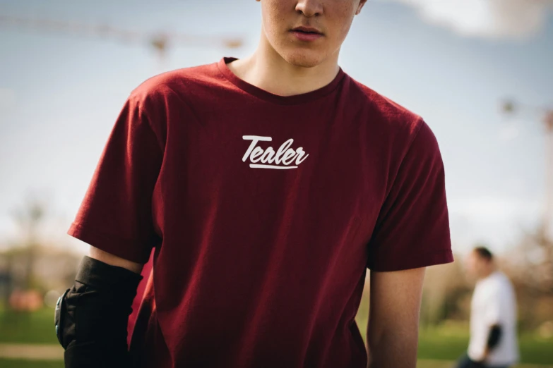 a young man wearing a red t - shirt stands on a baseball field with his team