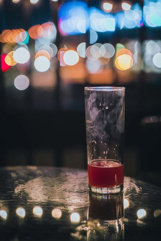 a glass of water and some drinks with lights in the background