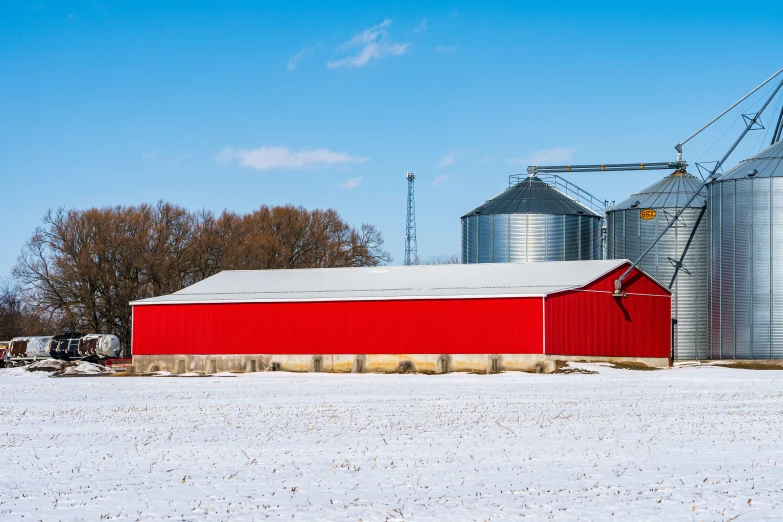 a barn sits next to a silo in a snowy field