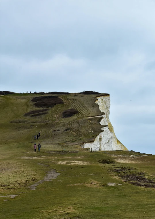 people are walking in the grass towards an old cliff