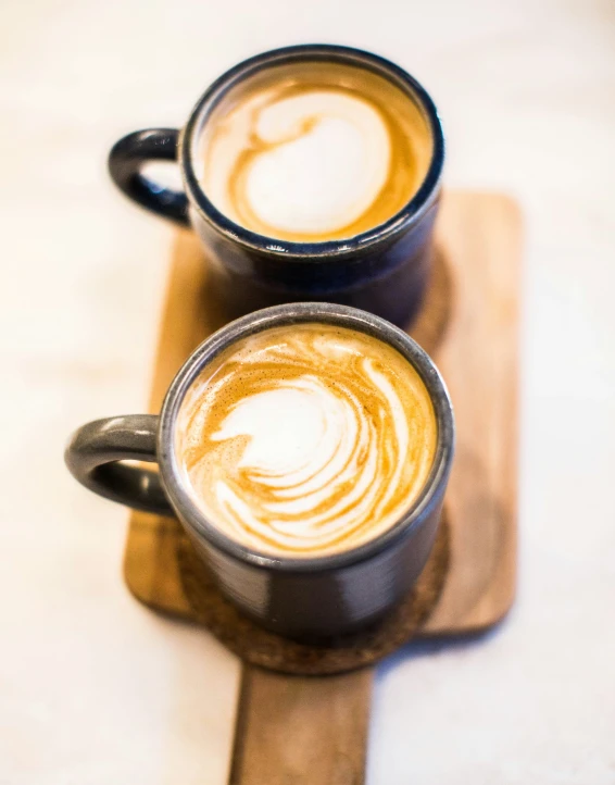 two cups of coffee sitting next to each other on a board