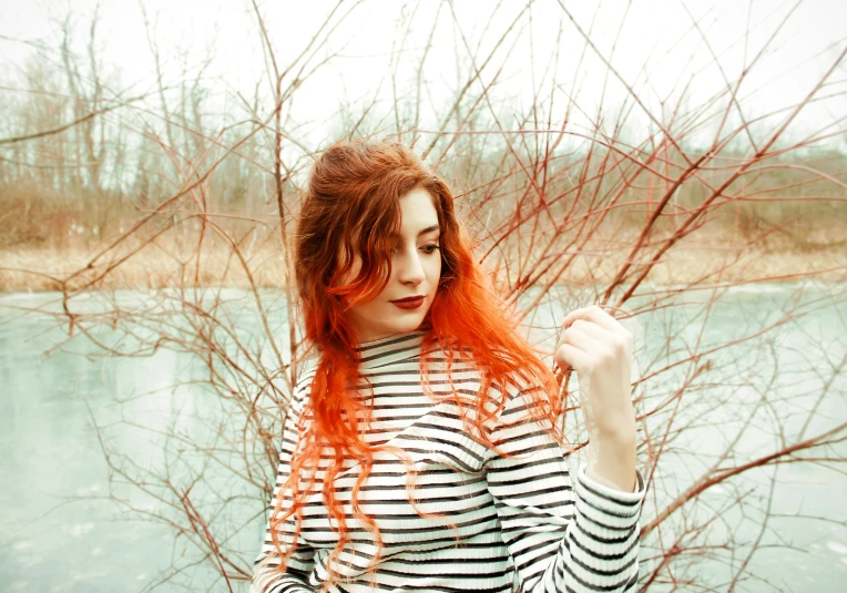 woman with orange hair posing by a body of water