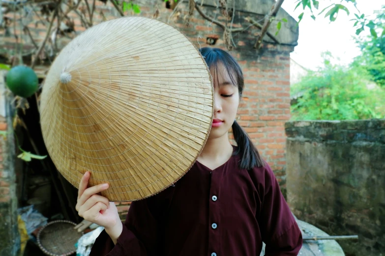 an asian woman in a maroon dress holding up a large bamboo umbrella