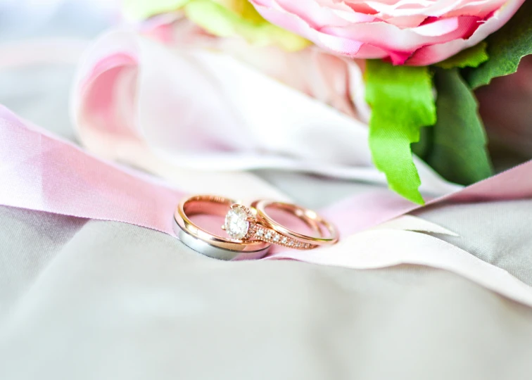 two diamond wedding rings resting on pink satin with a flower