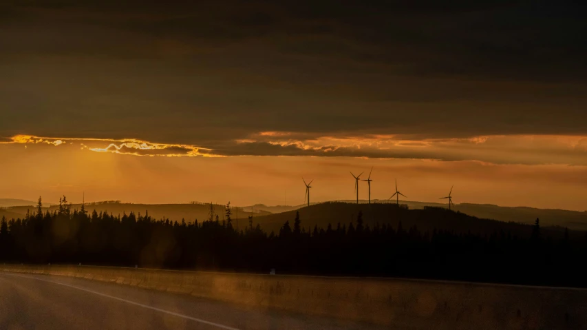 the sun is shining through the dark clouds behind wind mills