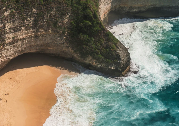 the view from above shows the ocean and sandy shoreline with a rocky wall at the bottom