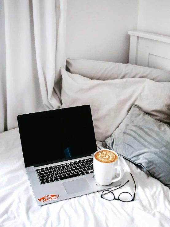 a laptop on a bed with a cup of coffee in front of it