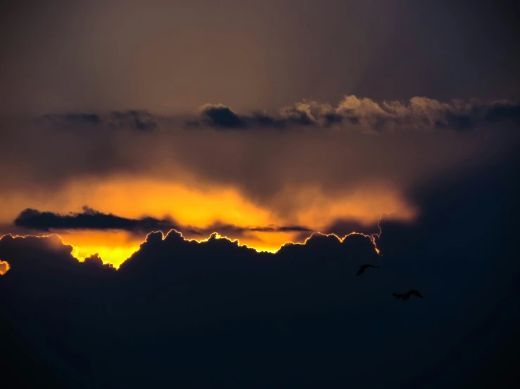 the sun sets behind some fluffy clouds