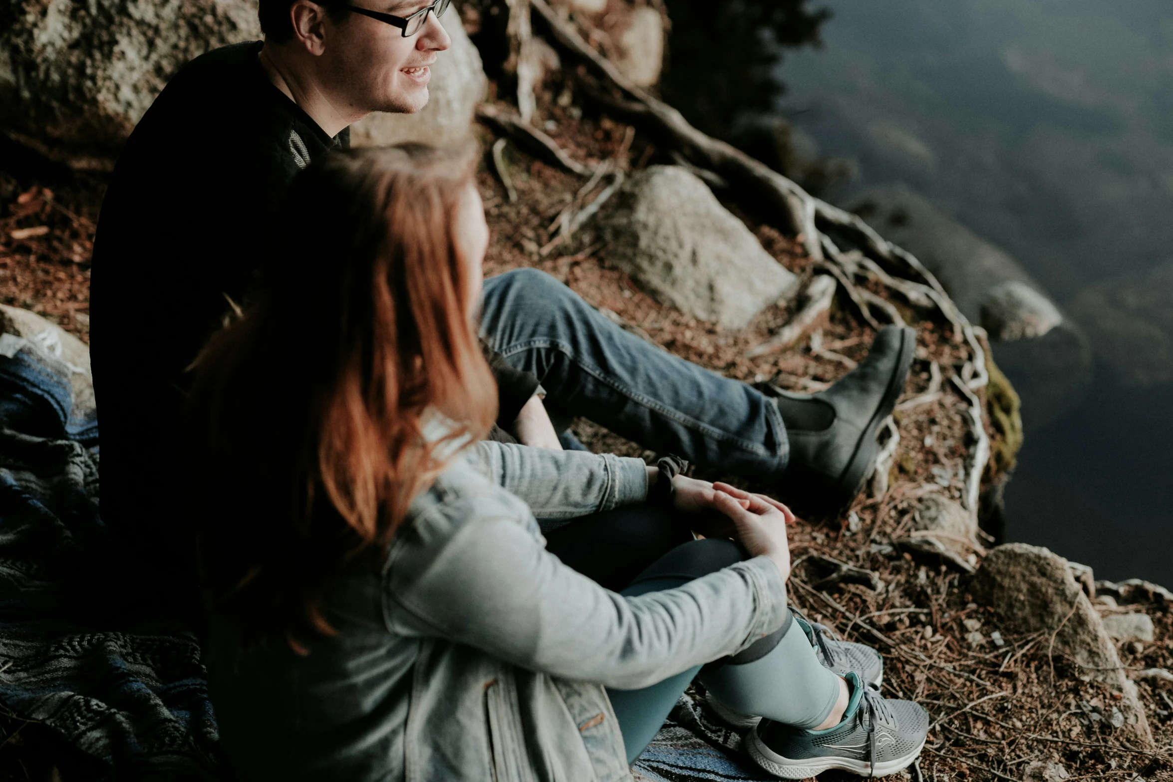 a man and woman are sitting on a mountain trail
