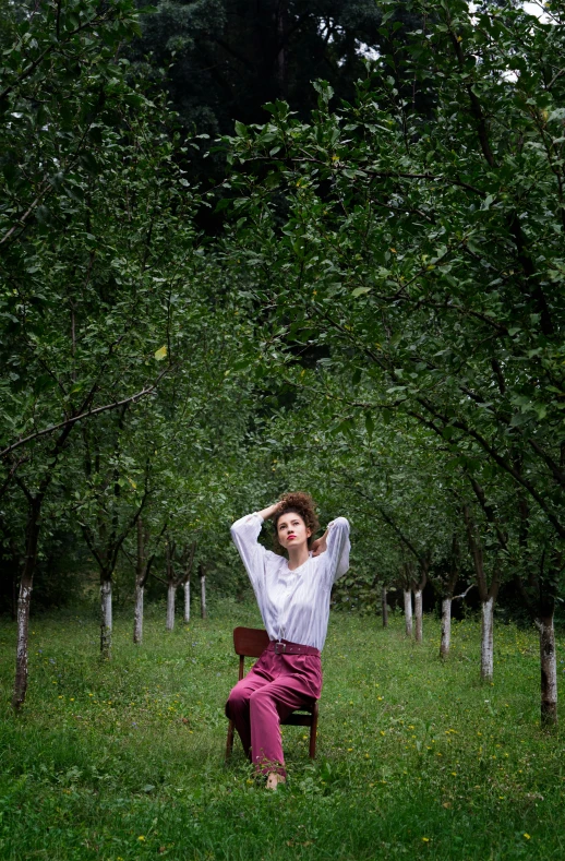 a woman wearing a white shirt is sitting on a chair in front of trees