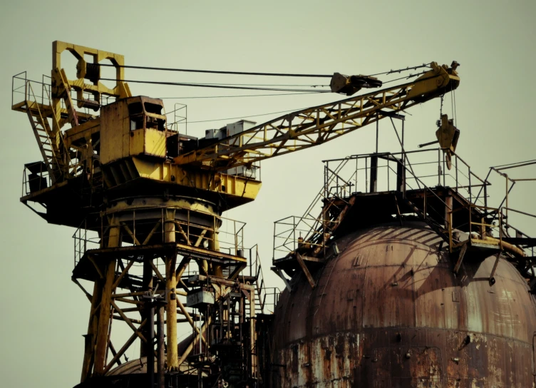 an old, rusty factory building with multiple large machinery items hanging off the tops of it