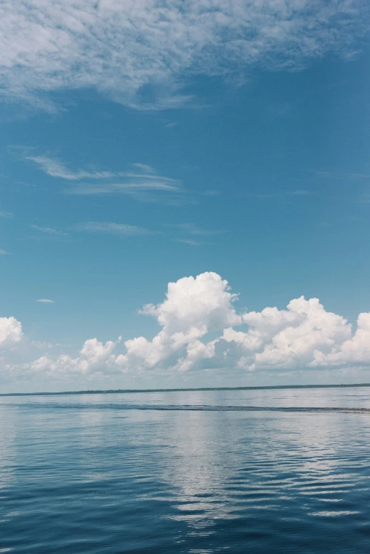 a lone boat floats in the water under a cloudy blue sky