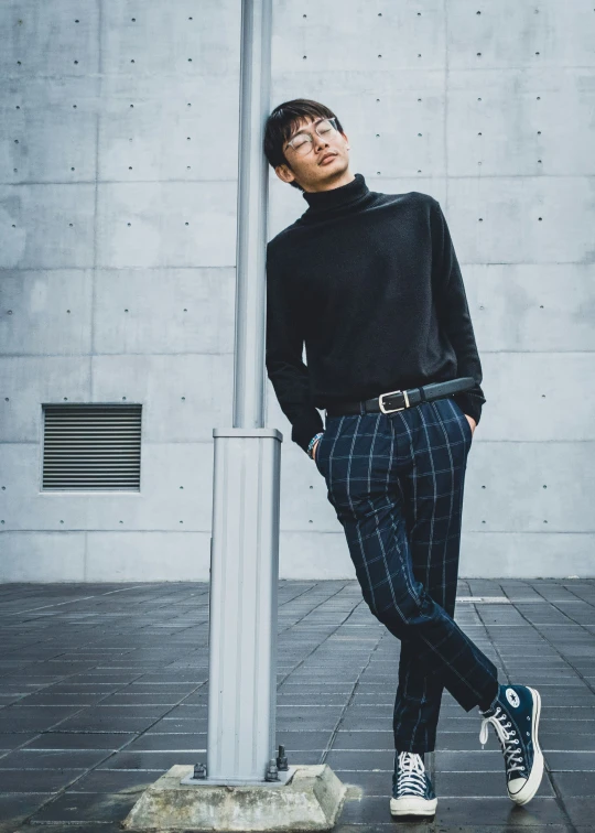 young man posing with a black top and blue pants