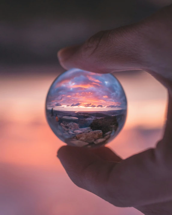 a hand holding up a sphere shaped with the sunset