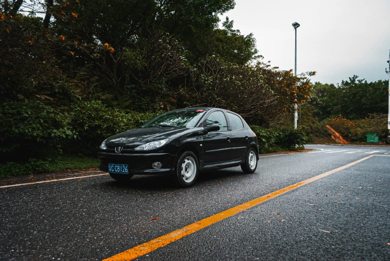 a black car driving down the road beside trees