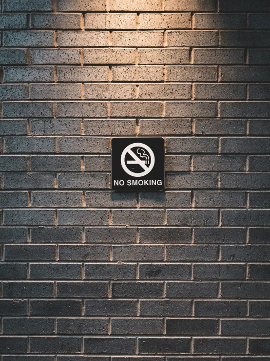 a no smoking sign is on a brick wall