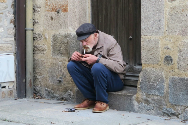 an old man that is sitting on the curb smoking a cigarette