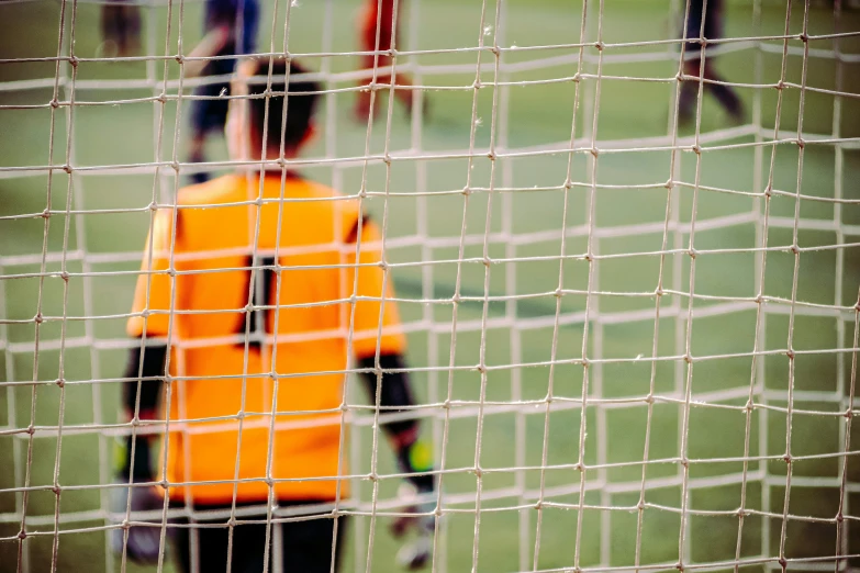 a young man with an orange vest on stands in front of the goal net