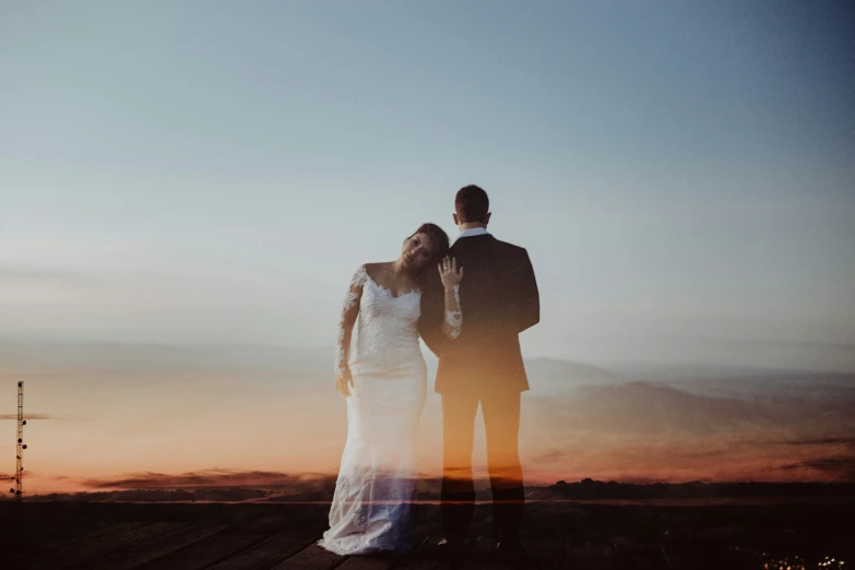 a bride and groom stand on the edge of a wooden dock