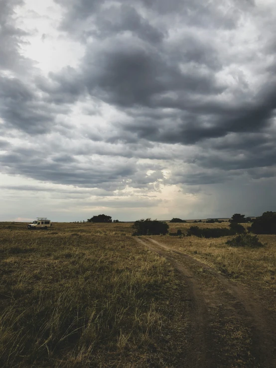 an open field with a truck on it under dark clouds