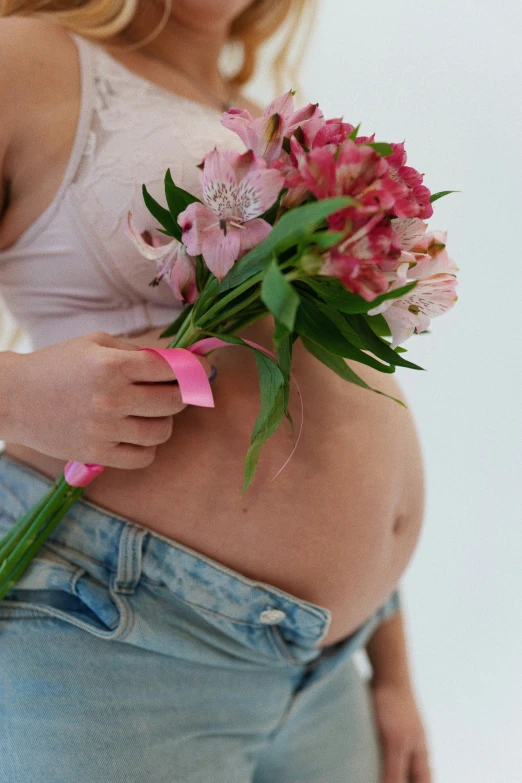 a pregnant woman with a pink ribbon around her waist is holding flowers