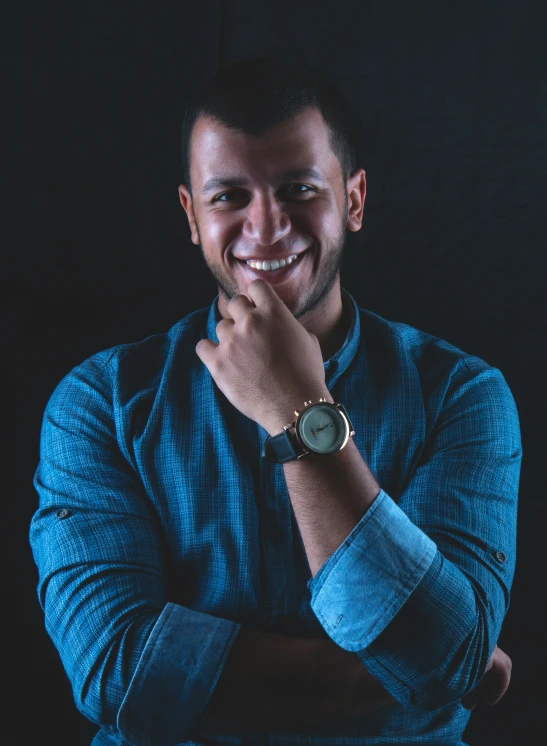 smiling man in blue shirt with his hands folded near his face