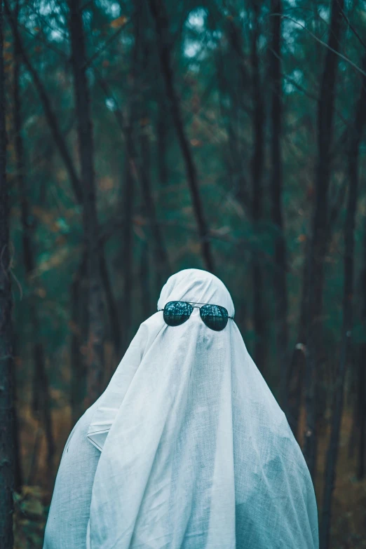 a man in sunglasses and ghost costume hiding in the woods