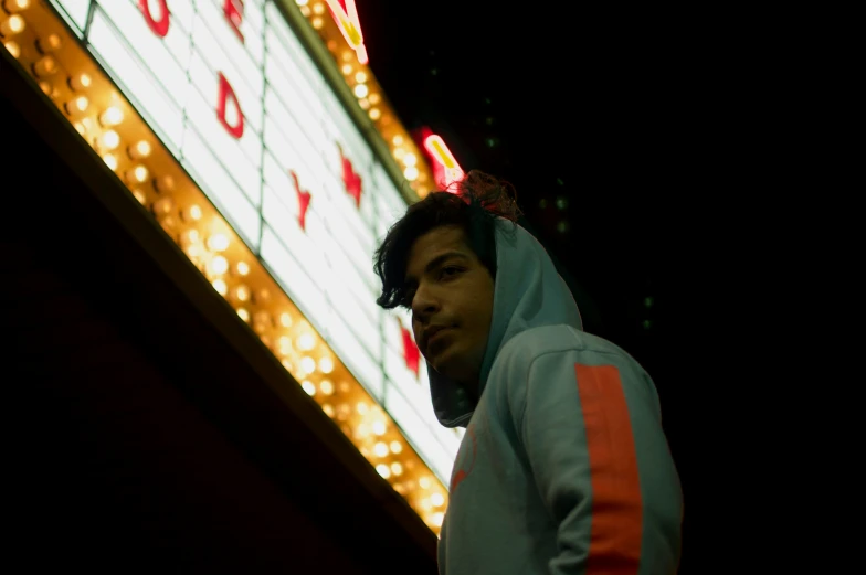 a man in a hooded sweatshirt standing by the las vegas sign