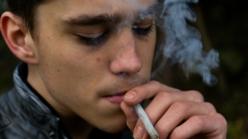 a man smoking with his eye closed and cigarette in hand