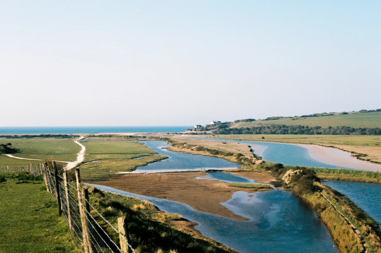 a wide river with grassy fields and an ocean beyond