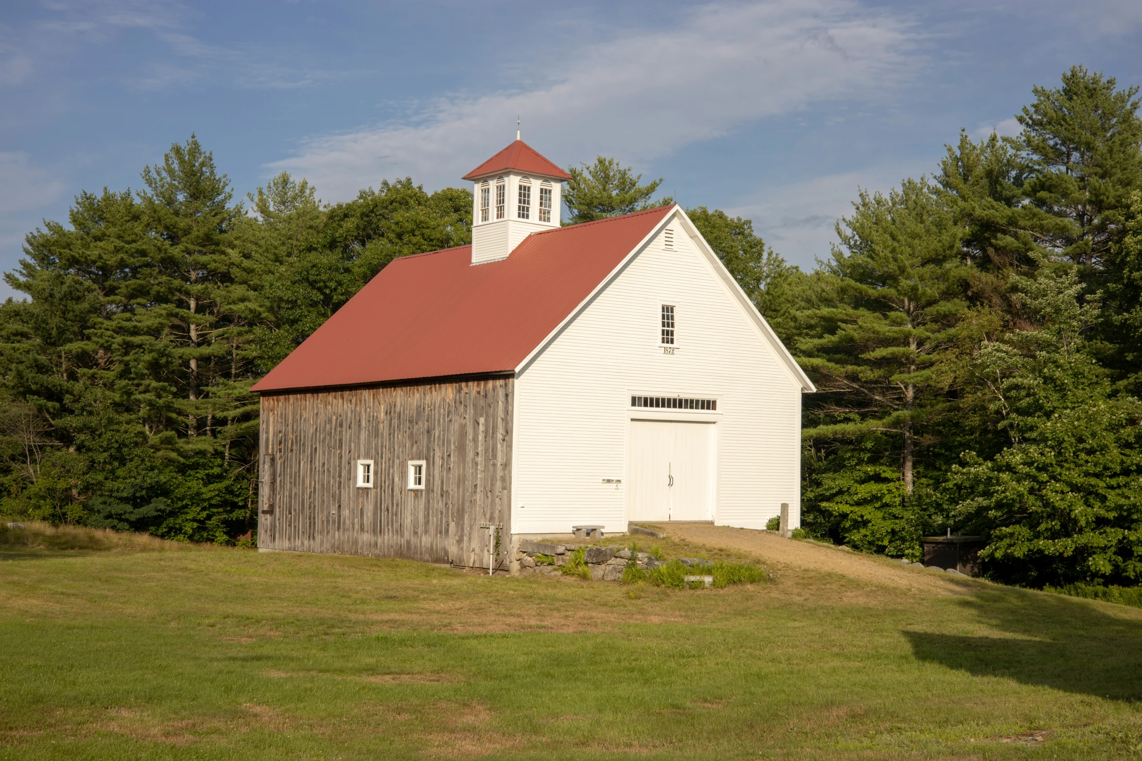 a small white building with a red roof surrounded by tall trees