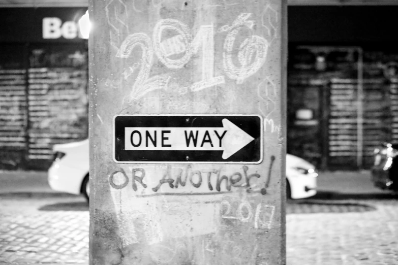 black and white pograph of one way sign with graffiti on it