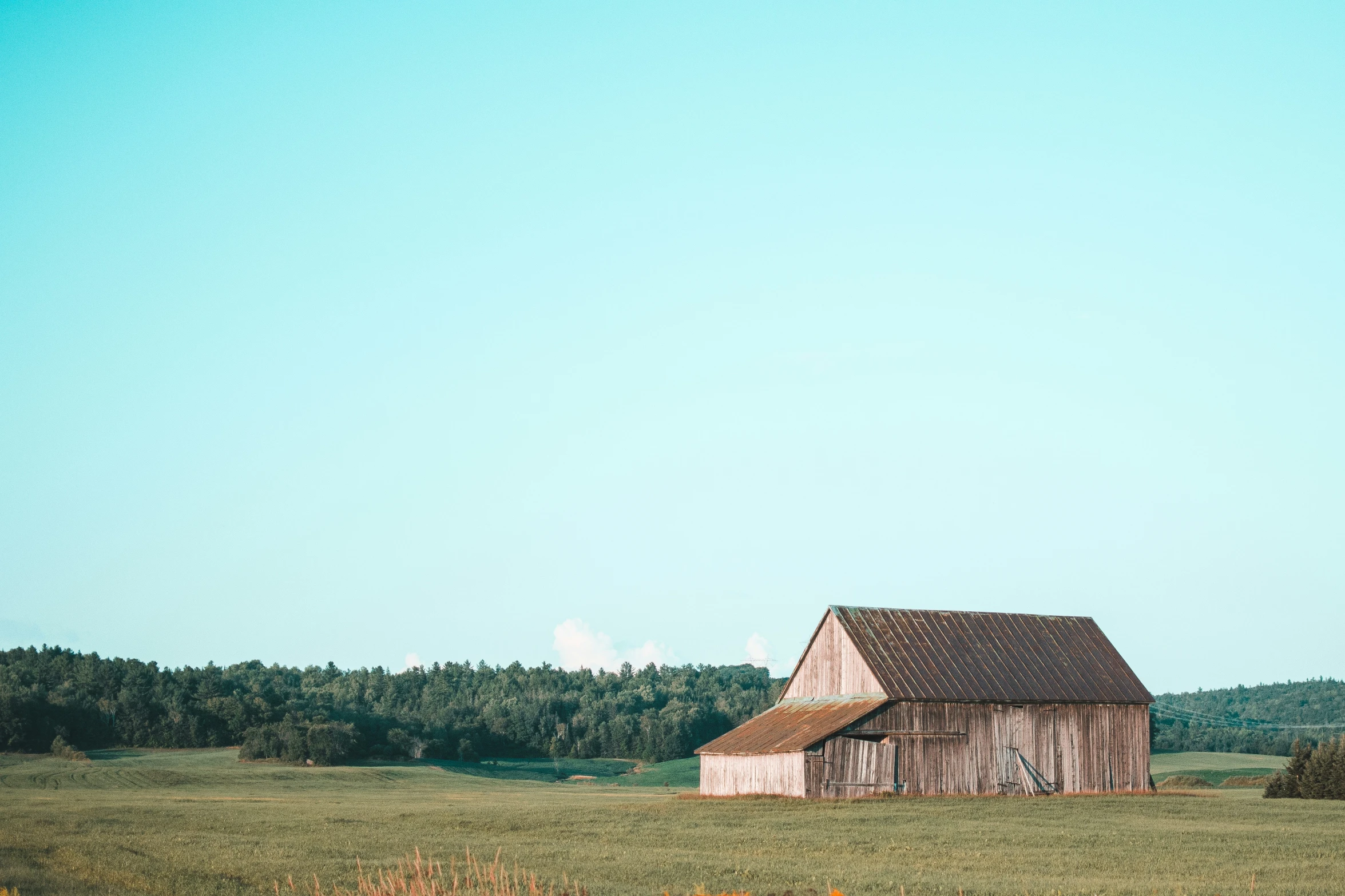 an old barn and hay field near a wooded area