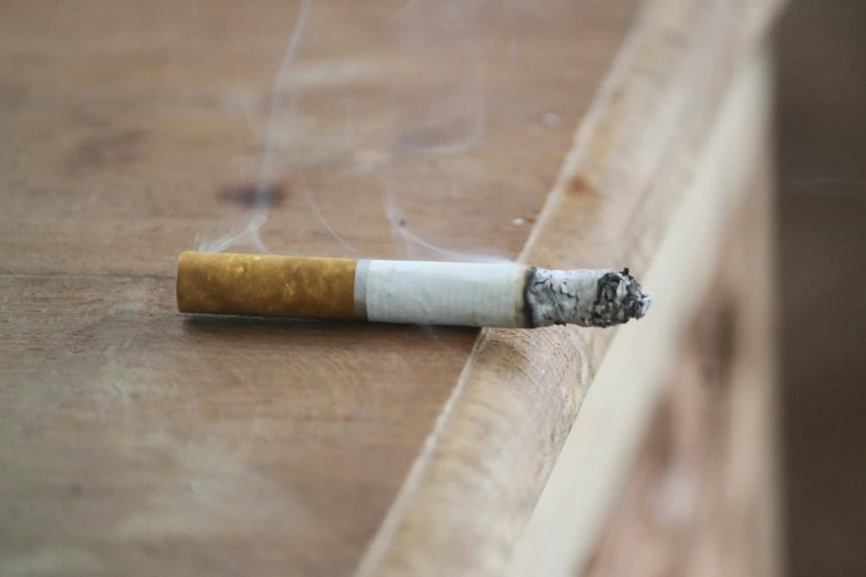 a single cigarette sticking out of the edge of a wooden floor