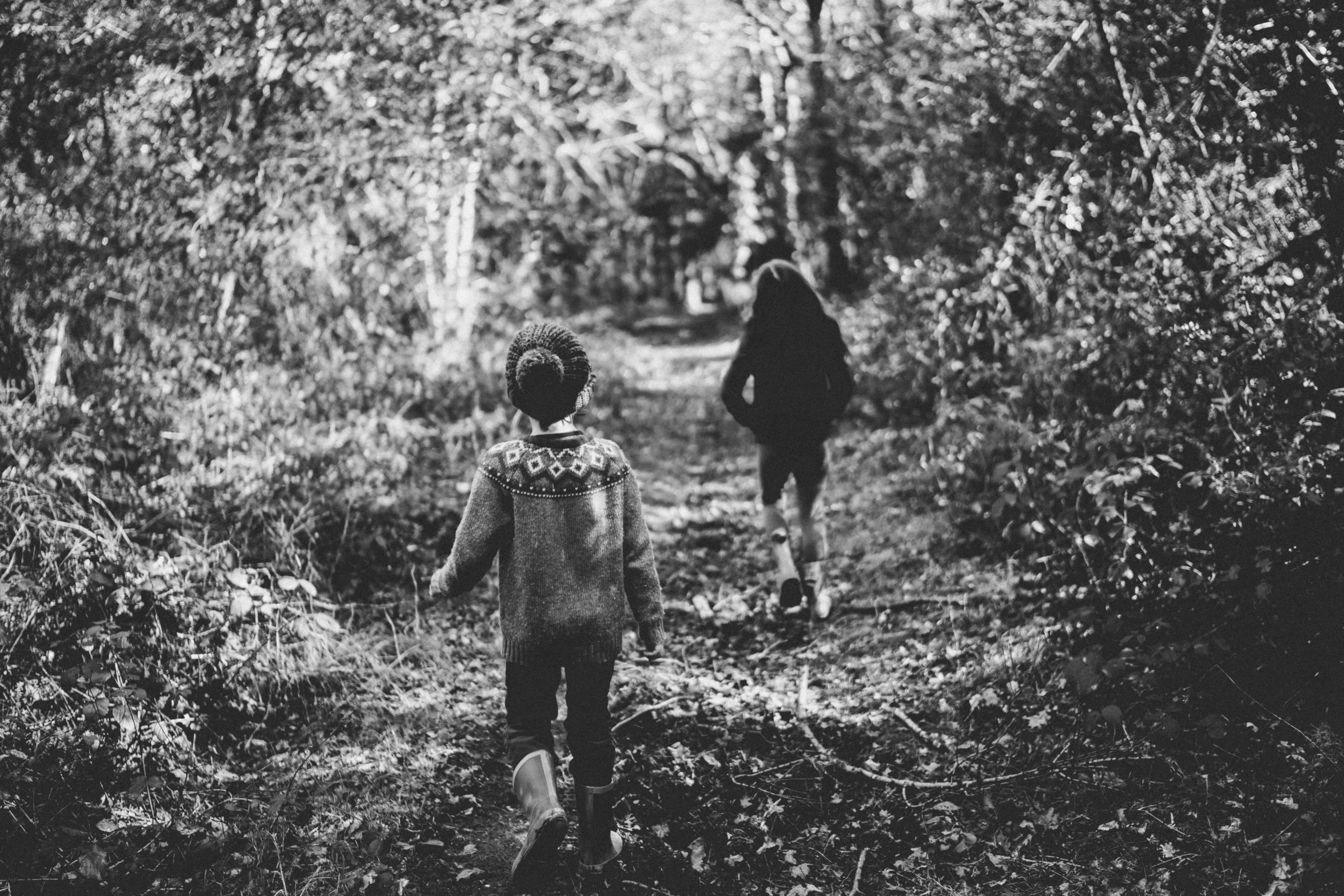 two people walk through a wooded path towards the camera