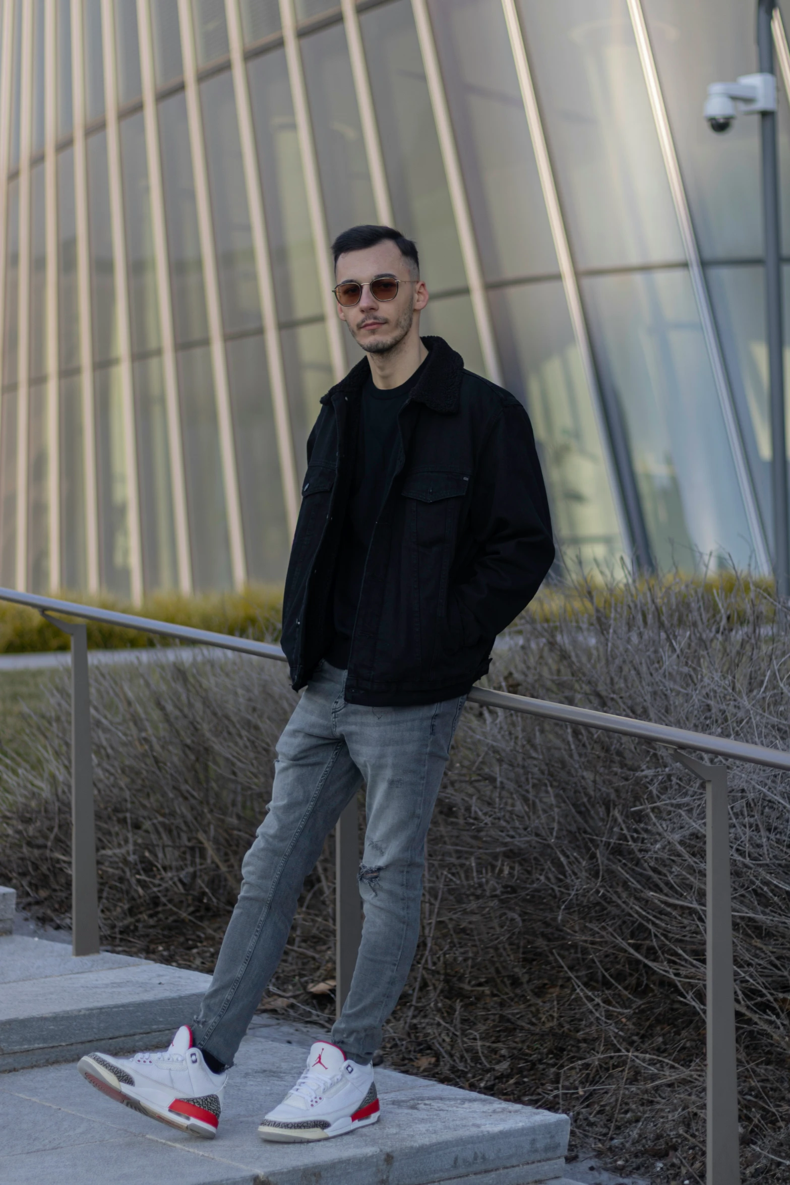 man with sunglasses, jeans, and a black jacket standing on some steps