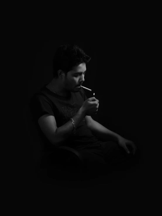 a man sitting in the dark, smoking a cigarette