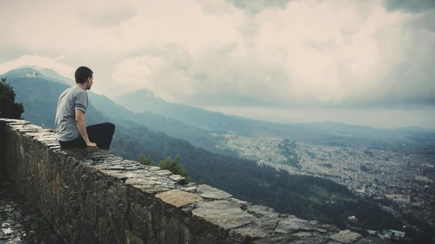 a man sitting on the ledge of a building looking over the mountains