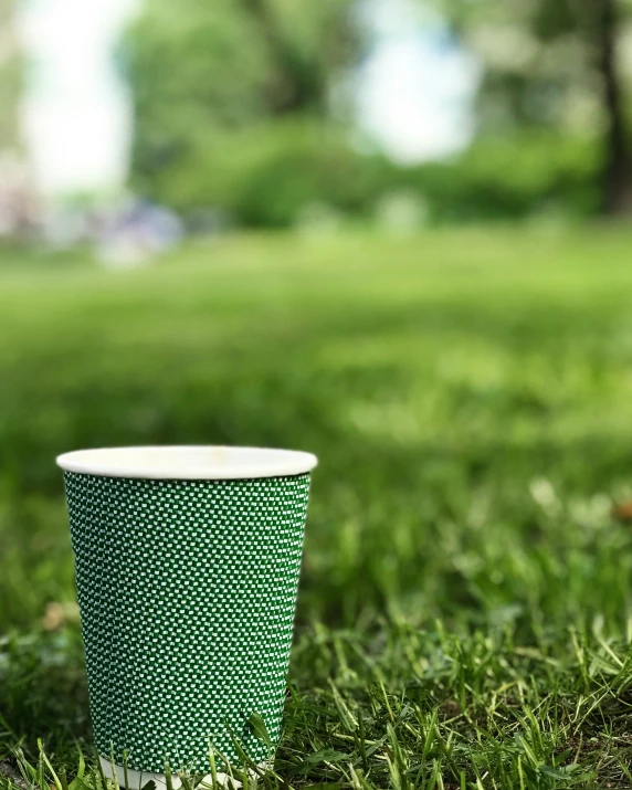 a green cup sitting on top of a grass covered field