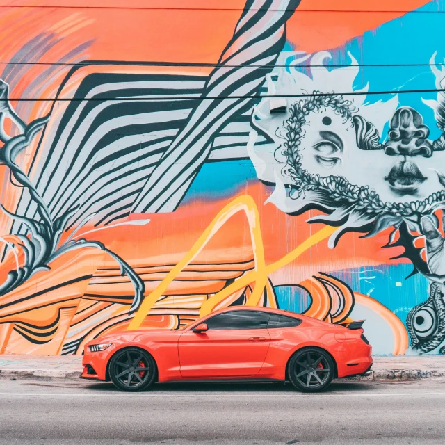 a car parked in front of a wall with an artistic painting
