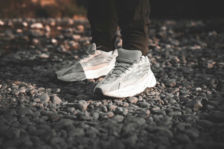 a person wearing white and gray sneakers standing in a rocky area