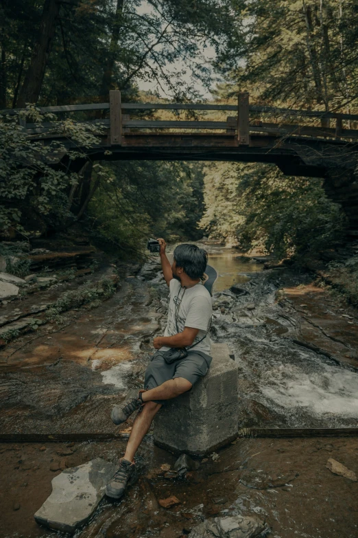 man sitting on rock in middle of stream