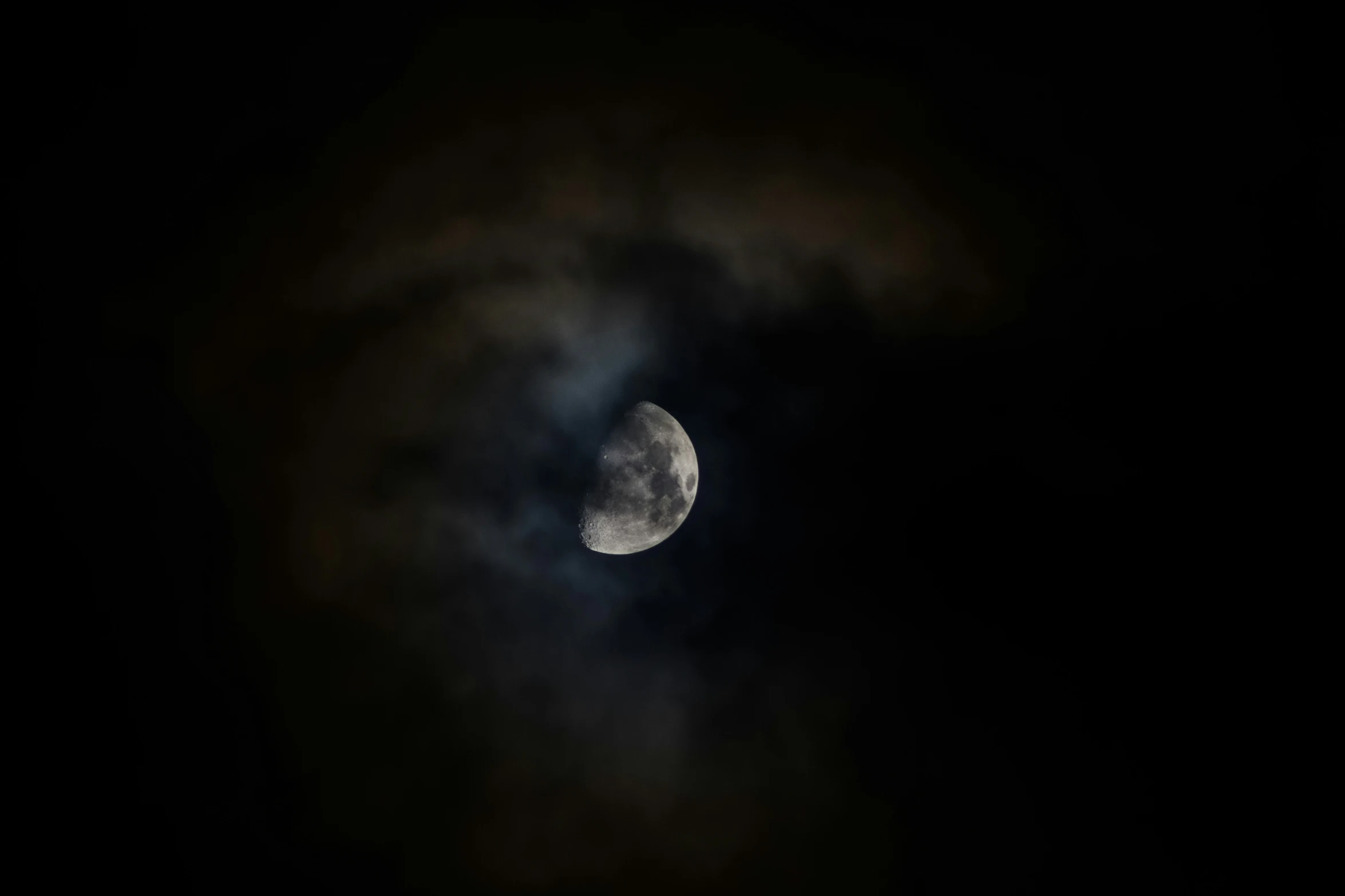 the moon is seen through a cloudy sky